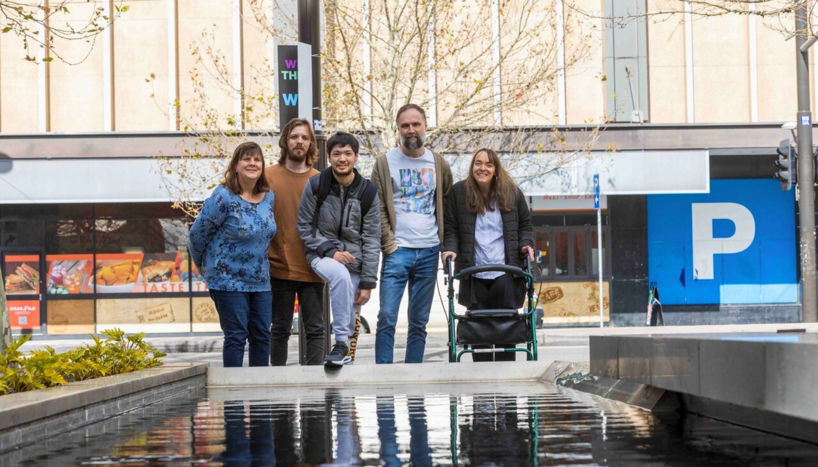 Five people are standing in front of a pond and smiling at the camera. Image supplied by City of Adelaide.