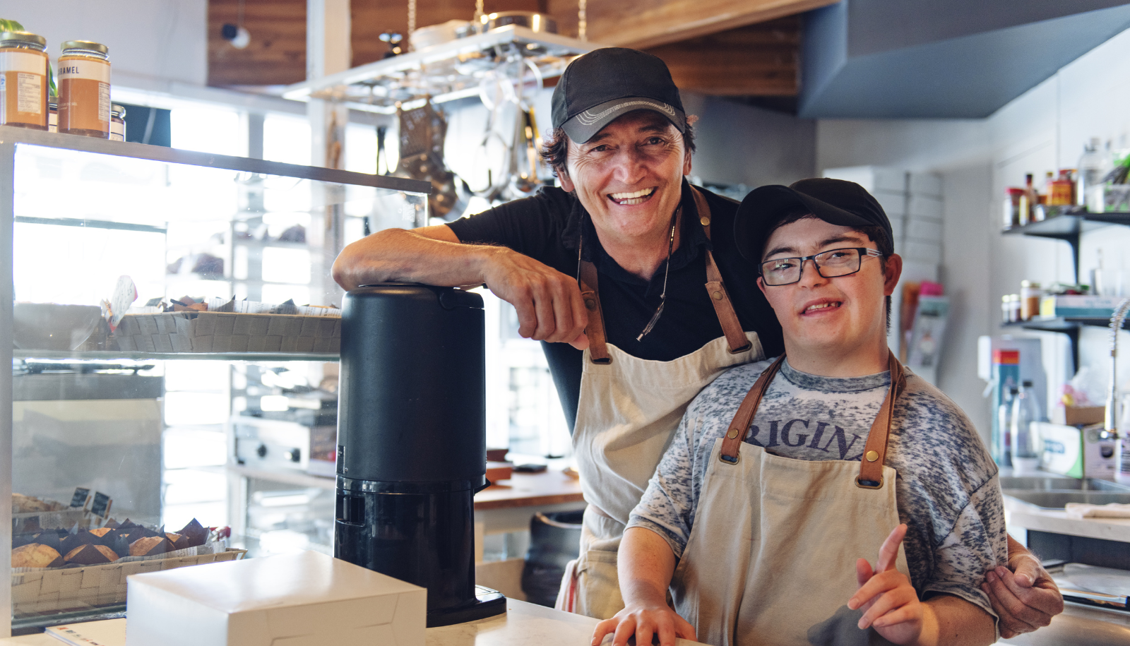 Two people working at a cafe smiling at the camera.