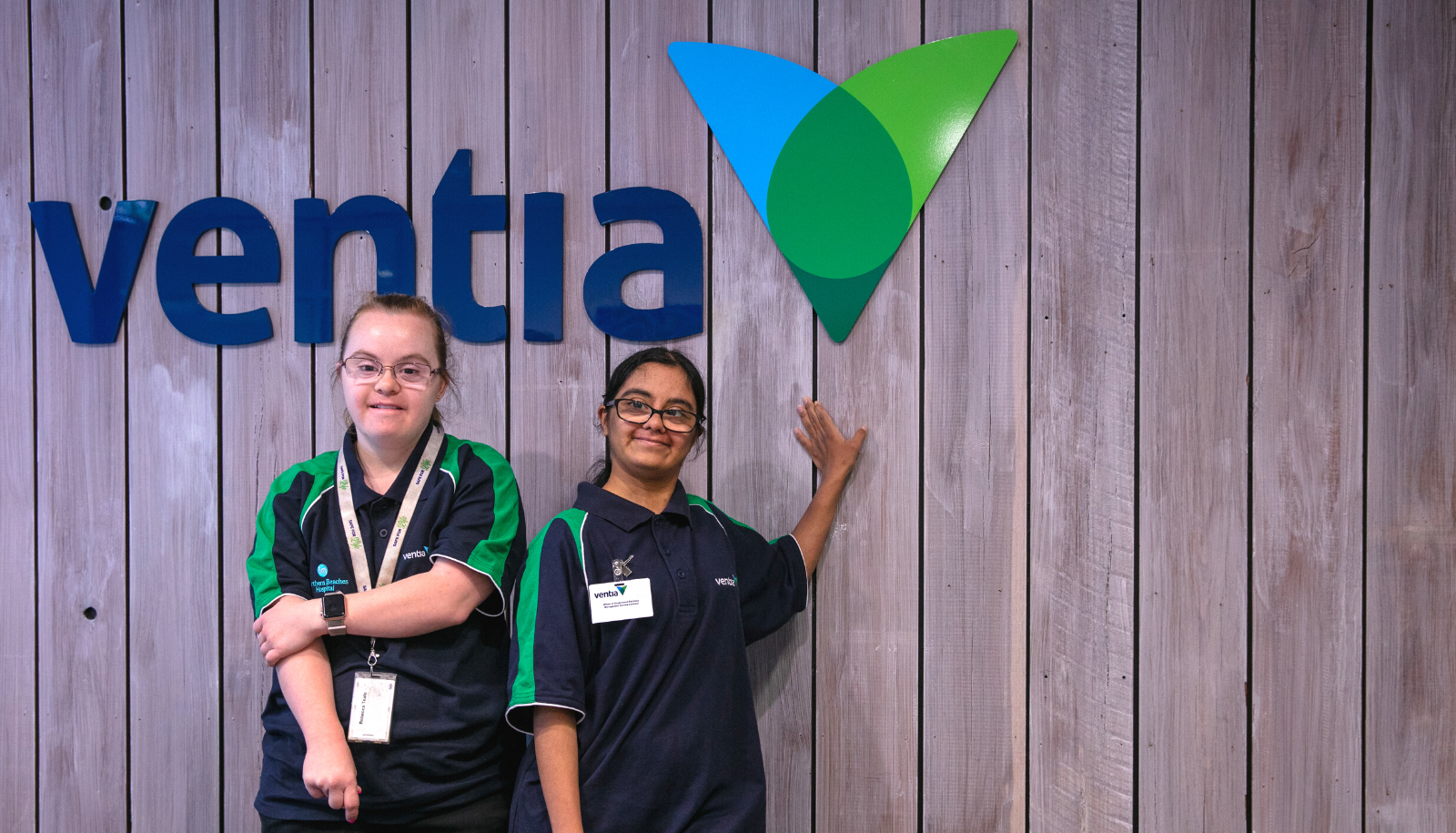 Two staff members at Ventia’s office standing in front of the company’s logo signage