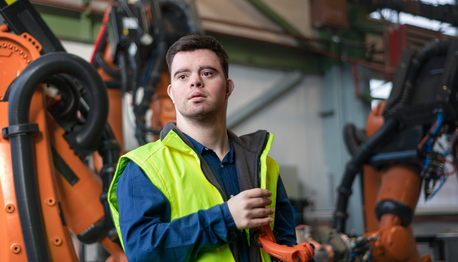 a young man wearing high-vis clothing working in a factory surrounded by machinery