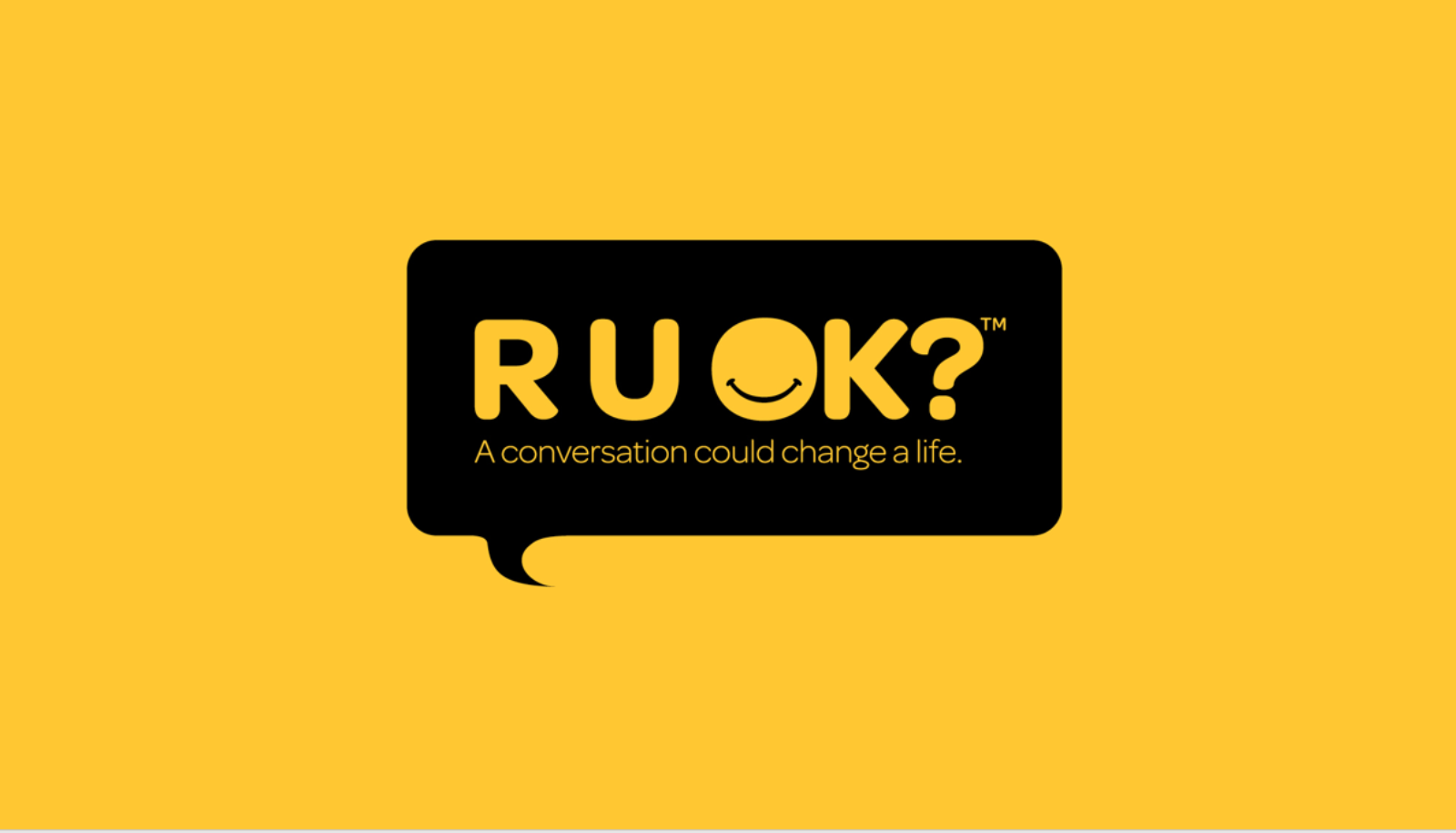 A black rectangular sign with text "R U OK? A conversation could change a life." and a yellow background.