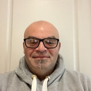 Michael standing in front of wall, wearing a jumper and glasses, smiling at camera.